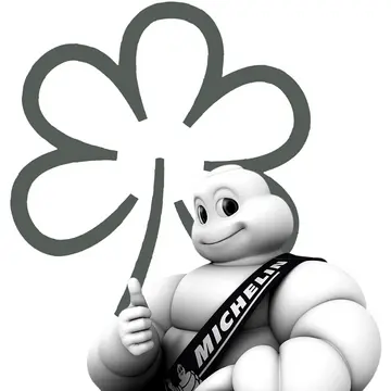 Der Michelin-Mann, auch bekannt als Bibendum, lächelt herzlich und hält eine stilisierte, schwarz-weiße Blume in der Hand, die das Engagement der legendären Reifenmarke für Qualität und Service in der Automobilindustrie symbolisiert. - Ihr Landhaus Scherrer aus Hamburg