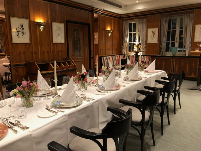 Ein elegantes Esszimmer für einen formellen Anlass, mit einem langen Tisch, geschmückt mit floralen Tischdekorationen, feinem Porzellan und ordentlich gefalteten Servietten, umgeben von klassischen schwarzen Stühlen, unter warmer Beleuchtung. - Ihr Landhaus Scherrer aus Hamburg