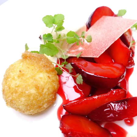 Ein goldbrauner, knuspriger Quarkknödel aus der Wilstermarsch, serviert mit glänzenden, geschnittenen roten Erdbeeren und einer cremigen Sauce, garniert mit einem zarten Kräuterzweig und einer dünnen, knusprigen Oblate im Restaurant Hamburg. - Ihr Landhaus Scherrer aus Hamburg