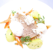 Ein Gourmetgericht mit Scheiben von gewürztem Fleisch, garniert mit geriebenem Käse, Sahnehäubchen und frischen Kräutern, serviert mit glasierten Karotten und Salzkartoffeln, kunstvoll angerichtet auf einem weißen Teller. - Ihr Landhaus Scherrer aus Hamburg