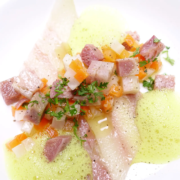 Ein farbenfrohes Gericht mit fein gewürfeltem Fleisch, möglicherweise Thunfisch, und buntem Gemüse, garniert mit frischen Kräutern und abgerundet mit einer zarten, schaumigen grünen Sauce und durchscheinenden Gelblättern. - Ihr Landhaus Scherrer aus Hamburg